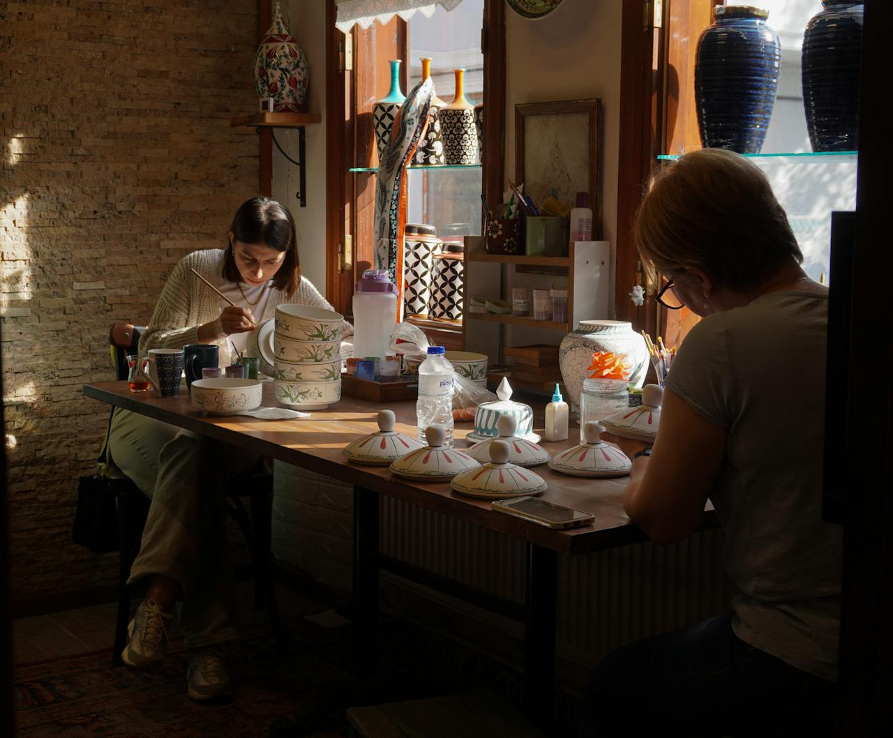Home Artists hand-paint intricate designs on ceramics in a sunlit workshop in Bursa, Türkiye.